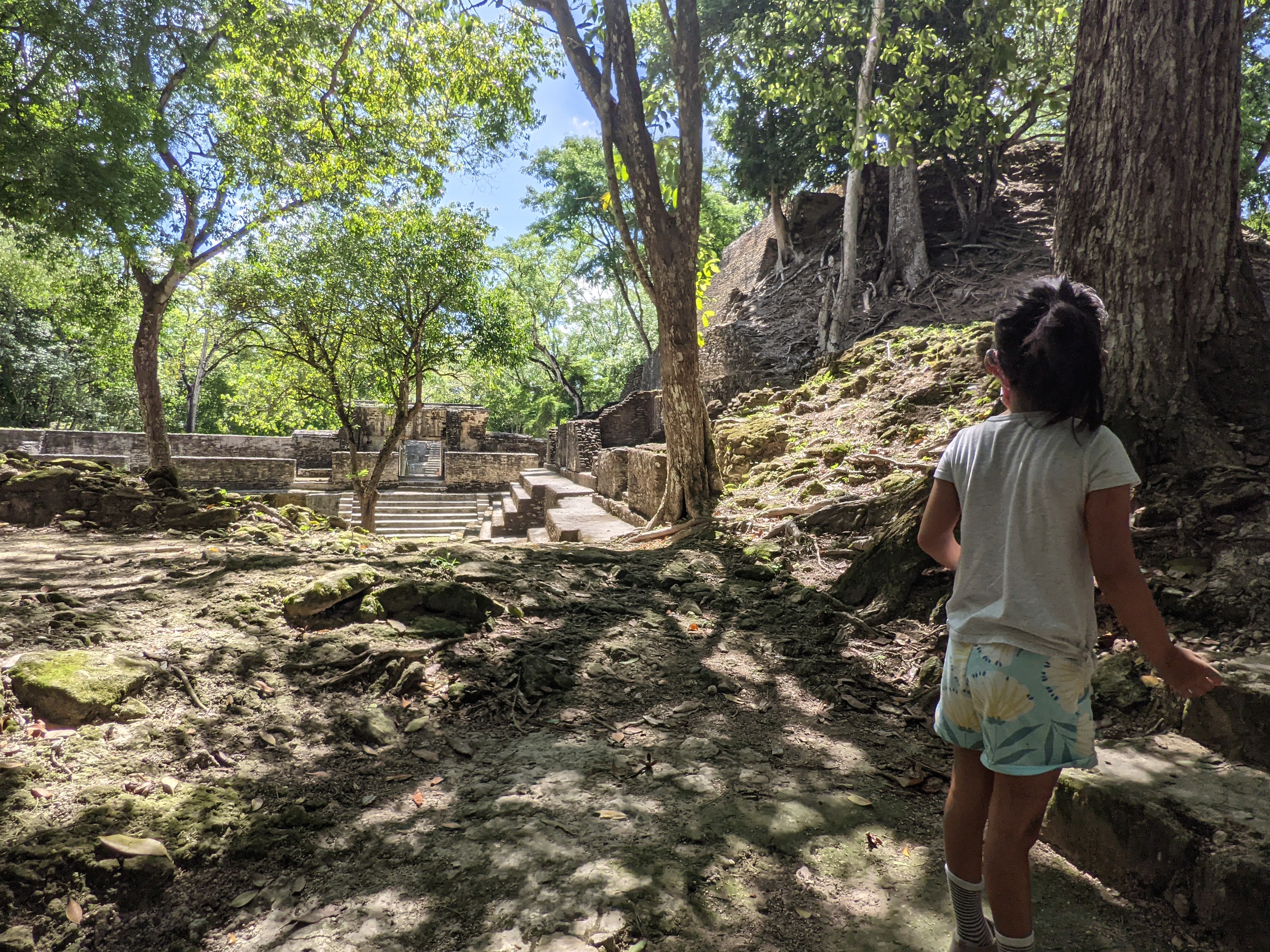 dark haired child in shorts and t-shirt standing infront of maya ruins.